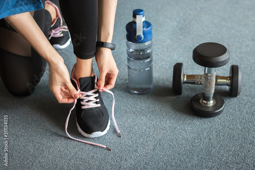Fitness woman tying shoelaces before exercise workout at gym Poster Mural XXL