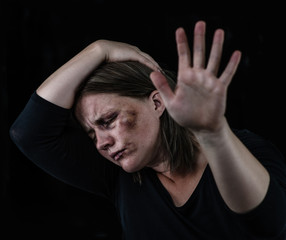 Wall Mural - Crying woman victim of domestic violence and abuse showing a stop sign with her hand. Isolated on dark background