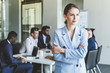 © xartproduction - Business woman stands on the background of partners. A team of young businessmen working and communicating together in an office. Corporate businessteam and manager in a meeting