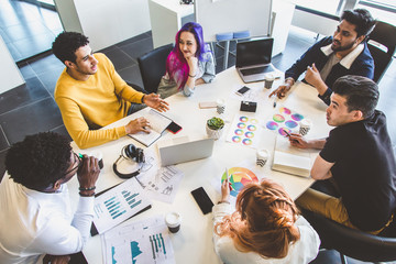 Wall Mural - Group of multi ethnic executives discussing during a meeting. Business man and woman sitting around table at office and smiling. A team of young creative designers