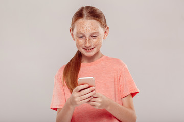 Wall Mural - Inclusive Beauty. Girl with freckles standing isolated on grey browsing internet on smartphone joyful