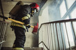 © alfa27 - young fireman in action, stand in landing, go to fight with fire, wearing uniform and holding hammer