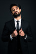 © xartproduction - Portrait of a young handsome successful Indian in a classic black three-piece business suit on a dark background, holding with both hands the jacket lapels