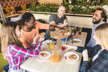 A company of multicultural  young people in a cafe eating pizza, drinking cocktails, having fun