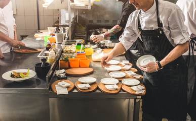 Wall Mural - Professional chef cooking in the kitchen restaurant at the hotel, preparing dinner. A cook in an apron makes a salad of vegetables and pizza.