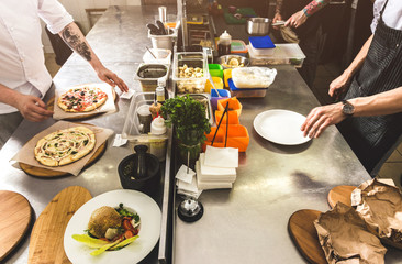 Wall Mural - Professional chef cooking in the kitchen restaurant at the hotel, preparing dinner. A cook in an apron makes a salad of vegetables and pizza.