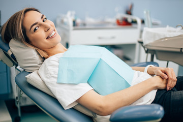 pleased patient after successful teeth treatment, lying in dental office and looking at camera. Medical equipment in the background