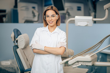 portrait of female dentist in white doctor's uniform standing in office near equipment and look at camera. Medicine, dentist, orthodontic concept