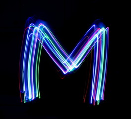 Wall Mural - Long exposure photograph of a letter m in neon colour in an abstract swirl, parallel lines pattern against a black background. Light painting photography.