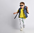 canvas print picture - Attractive little boy in stylish warm clothes with a backpack on his shoulders, having fun on a light studio background.