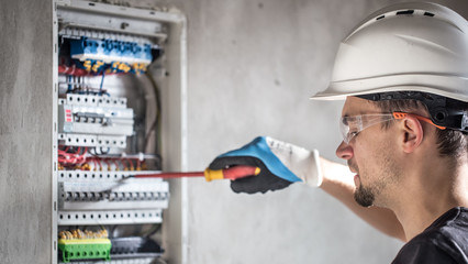 Man, an electrical technician working in a switchboard with fuses. Installation and connection of electrical equipment.