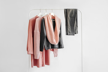 Female clothes in pastel pink and gray color on hanger on white background.  Jumper, shirt, jeans and scarf. Spring/autumn outfit. Minimal concept.