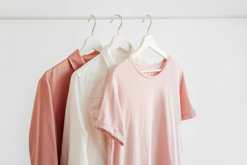 Wall Mural - Feminine clothes in pastel pink color on hanger on white background. Elegant dresses and shirt. Spring/summer outfit. Minimal concept.