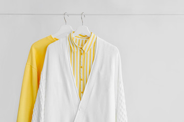 Wall Mural - Female clothes in yellow color on hanger on white background. Jumper and striped shirt. Spring/autumn outfit. Minimal concept.