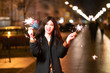 © Alex - beautiful girl with sparklers in the evening on the street. festive mood sparkling hand-held fireworks.