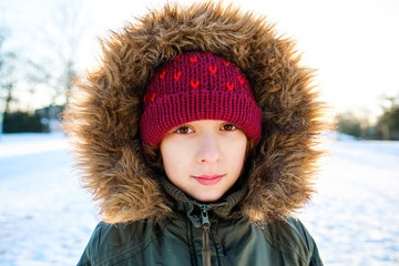 Wall Mural - Winter portrait of beautiful kid girl with fur hood outdoors. Family leisure with children on cold snow days. Happy young child have fun with snow on nature. Girl dressed a green coat and red hat.