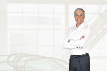 Wall Mural - Mature businessman portrait with his arms folded, in high key modern office setting.