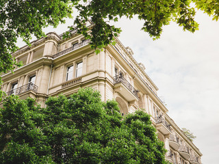 View through green trees of dream parisian apartment building real estate in France haussmannian architecture