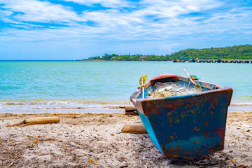 Wall Mural - Old blue wooden fishing boat docked on sea shore/ seashore on white sand beach coast landscape with empty fish nets and paddles mounted/ rolled on a log. Sunny summer day on tropical Caribbean island.