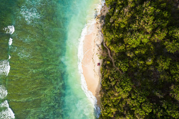 Wall Mural - View from above, stunning aerial view of some tourists sunbathing on a beautiful beach bathed by a turquoise rough sea during sunset, Green Bowl Beach, South Bali, Indonesia.