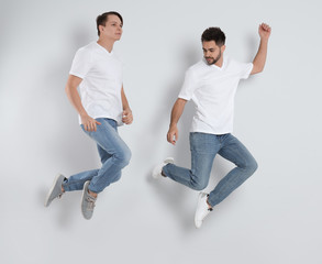 Wall Mural - Young men in stylish jeans jumping on light background