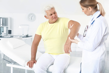 Sticker - Doctor examining mature man with joint pain in clinic