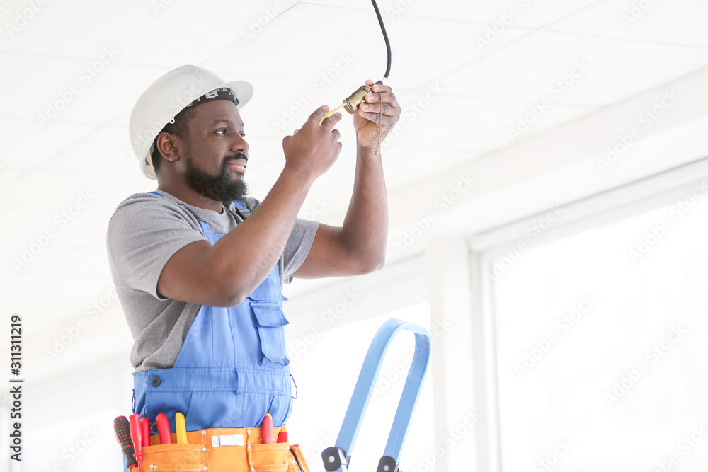African-American electrician performing wiring in room