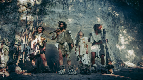 Cuadros en Lienzo Tribe of Four Hunter-Gatherers in Animal Skin Holding Stone Tipped Tools, Pose at Entrance of their Cave