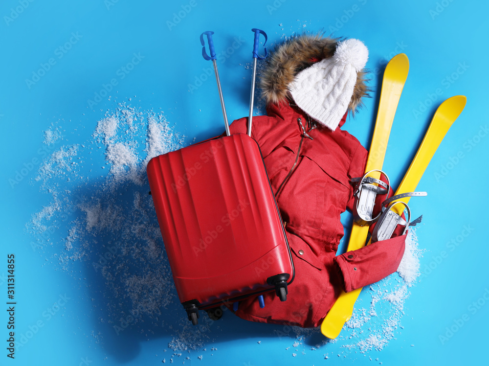 Suitcase with warm clothes and skis on light blue background, flat lay. Winter vacation - obrazy, fototapety, plakaty 