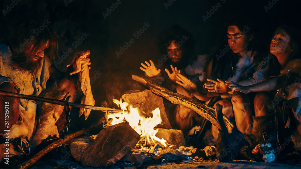 Neanderthal or Homo Sapiens Family Cooking Animal Meat over Bonfire and then Eating it. Tribe of Prehistoric Hunter-Gatherers Wearing Animal Skins Eating in a Dark Scary Cave at Night - obrazy, fototapety, plakaty 