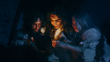 Fototapeta Zwierzęta - Tribe of Prehistoric, Primitive Hunter-Gatherers Wearing Animal Skins Use Digital Tablet Computer in a Cave at Night. Neanderthal or Homo Sapiens Family Browsing Internet, Watching Videos, TV Shows 
