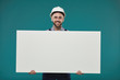 © Seventyfour - Horizontal studio portrait shot of happy young adult manual worker holding blank poster looking at camera smiling, blue turquoise background