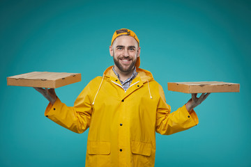 Horizontal waist up portrait of pizza man wearing bright yellow uniform holding two pizza boxes against blue turquoise wall background