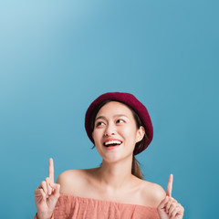 Portrait of confident beautiful asian woman with hand pointing up and looking up isolated on blue color background with studio shot.Skincare for healthy face concept.