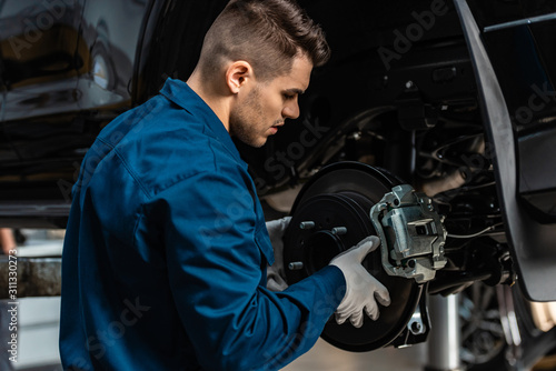 Cuadros en Lienzo young, attentive mechanic installing disc brakes on raised car