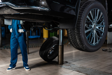 Wall Mural - cropped view of mechanic standing near car raised on car lift