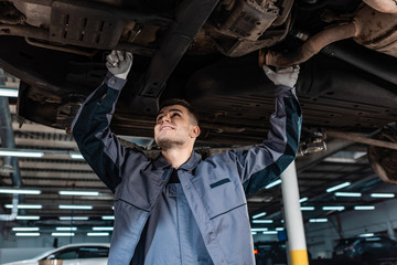 Wall Mural - smiling mechanic inspecting bottom of raised car with wrench