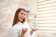 © borevina - A beautiful young brunette nurse laughs and looks at the camera while she has a green body care gel in her hands. She is at a new and modern medical body care clinic. Copy space.