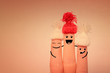 Fingers with painted faces in red knitted hats hug and smile on a pink background. Happy family concept. Copy space