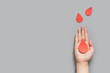 Blood donation - Human hand holding blood drop symbol on gray background with copy space. World blood donor day and save life concept. Flat lay.