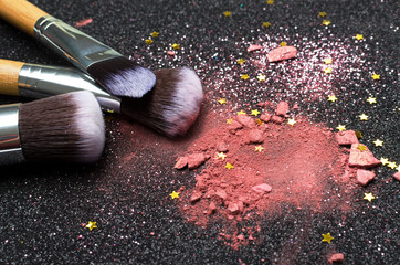 Closeup of pink blusher, glitter, decorative golden stars for make up and brushes kit on the black background.Concept of makeup for party