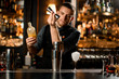 © fesenko - Male bartender pouring a liqour from the jigger to a professional steel shaker