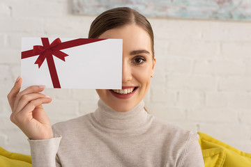 Wall Mural - Beautiful girl covering face with gift card template and smiling at camera