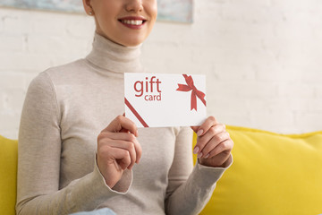 Wall Mural - Cropped view of smiling woman showing gift card on couch