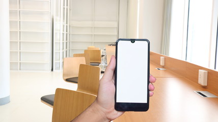 Hand holding blank screen smart phone over modern conference room with Wooden table and wooden chair background.