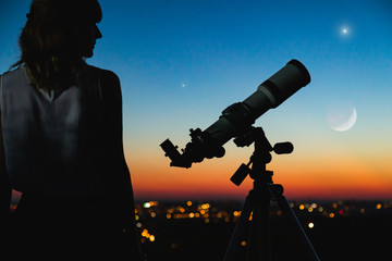 Wall Mural - astronomer with a telescope watching at the stars and moon with blurred city lights in the backgroun