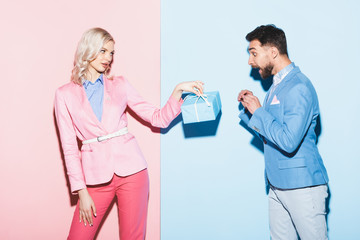 Wall Mural - attractive woman giving present to shocked man on pink and blue background