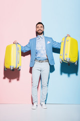 Wall Mural - smiling man holding travel bags on pink and blue background