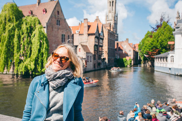 Wall Mural - A beautiful young girl sits on the background of a famous tourist spot with a canal in Bruges, Belgium