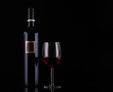 Fototapeta Panele - Closed red wine bottle with empty label and glass of wine on black background with reflections. Concept sales, discount price. Photo for advertising